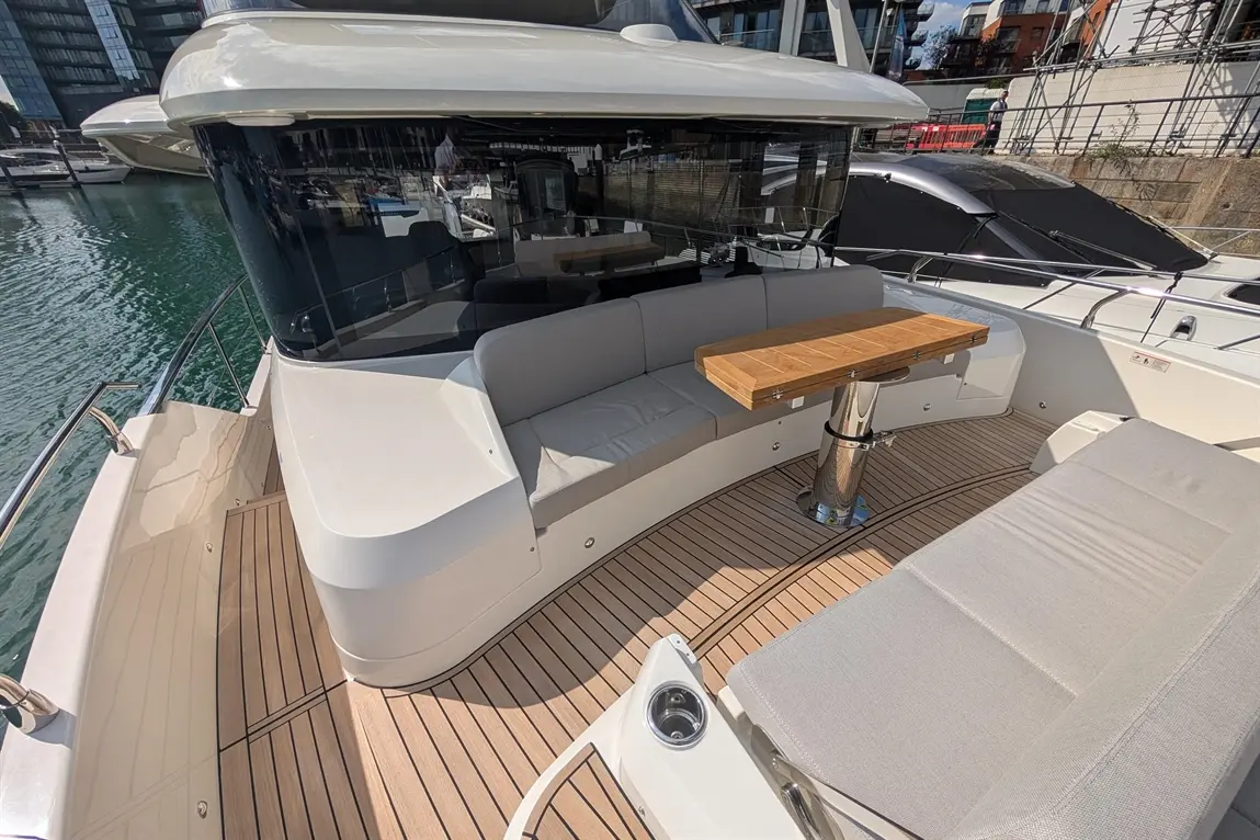 Modern yacht deck with grey cushioned seating, a wooden table, and a scenic water view in a marina.